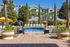 Inviting swimming pool area with sun loungers, elegant palm trees, and charming umbrellas in front of modern apartment complex.