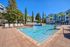 Inviting outdoor pool area with sun loungers, surrounded by lush greenery and modern apartment buildings under a clear blue sky.