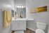 Elegant modern bathroom featuring sleek white cabinetry, polished countertop, soft yellow accents, and chic wall art.