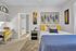Inviting bedroom with vibrant decor featuring a cozy bed, modern artwork, and natural lighting, leading into a bright bathroom.