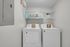 Modern laundry room with full-size washer and dryer, featuring stylish shelving and chic decor for a functional yet fashionable space.