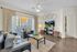 Bright and inviting living room featuring modern decor, cozy black leather seating, stylish glass coffee table, and a large window with elegant curtains.