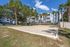 Charming apartment complex with tropical landscaping and a spacious sand volleyball court under clear blue skies.
