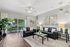 Bright and modern living room featuring sleek black leather sofas, elegant glass coffee table, and natural light streaming through large sliding doors to a lush outdoor patio.