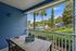 Charming patio with a wooden dining set offering a picturesque view of lush greenery and a sparkling pool, perfect for relaxation and outdoor dining.