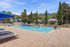Luxurious apartment complex featuring a sparkling outdoor pool with lounge chairs and shaded cabanas, surrounded by lush greenery and sophisticated architecture.