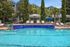 Luxurious pool area with crystal-clear water and stylish lounge chairs surrounded by lush trees and modern buildings.