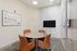 Sleek meeting room with modern design featuring a round granite table, comfortable orange chairs, and a wall-mounted TV.