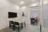 Modern meeting room with sleek TV, stylish stone accent wall, elegant table with four chairs, and an adjoining workspace featuring colorful seating options.