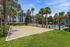 Charming apartment complex with a refreshing poolside area and a well-maintained sand volleyball court, surrounded by lush palm trees and greenery.