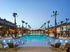 Luxurious apartment complex pool area at dusk, featuring palm trees, elegant lounge chairs, and inviting ambiance lighting.
