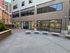 Modern urban plaza with stylish benches and large glass windows on a contemporary office building, offering a bright and inviting entrance.