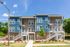 Modern apartment building with stylish blue and beige facade, surrounded by lush greenery and bright skies.