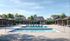 Luxurious community pool area with modern cabanas, surrounded by lush greenery and charming houses, under a clear blue sky.