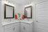 Elegant corner bathroom with dual sinks, modern mirrors, chic lighting, and vibrant orange towels accentuating a clean, sophisticated design.