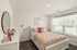 Bright and inviting bedroom with a floral-patterned bedspread, airy window view, and elegant decor on dresser.