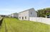 Charming backyard with lush green lawn and a modern, light-colored house surrounded by a white fence, perfect for outdoor enjoyment.