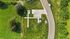 Aerial view of an idyllic property with lush green landscaping, modern driveway, and scenic surroundings along a curved road.