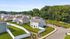 Charming suburban neighborhood with modern homes, lush green lawns, and scenic wooded backdrop on a sunny day.