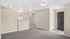 Modern apartment interior featuring an open-concept living area with beige walls, plush carpeting, and a ceiling fan overlooking a compact kitchen with white appliances.
