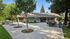 Charming outdoor patio area with shaded seating, a BBQ grill, and lush greenery surrounding a cozy single-story home.