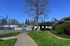 Charming apartment overlooking lush greenery and tennis court, featuring a picturesque path under a clear blue sky.