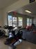 Inviting home gym with modern exercise bike, stability balls, kettlebells, and natural light streaming through large windows.