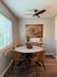 Bright dining area with modern round table, cozy leather chairs, and artistic wall decor, bathed in natural light.