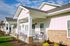 Charming single-story home with inviting front porch, white siding, and cozy seating area under a clear blue sky.