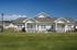 Charming duplex with modern white siding set against a clear blue sky, featuring inviting front porches and beautifully manicured lawns.