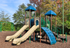 Colorful playground with dual slides, climbing structures, and swingset surrounded by lush greenery.