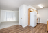 Inviting open-concept kitchen with wood flooring leading into a sunlit living area, featuring contemporary white appliances and ample storage.