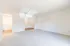 Spacious living area with carpeted flooring, white walls, and ample natural light.