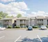 Sunny day view of modern apartment complex with well-maintained parking area and lush greenery.