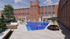 Charming urban oasis featuring a historic red brick building with a luxurious outdoor pool, surrounded by elegant lounge seating and lush greenery.