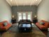 Bright and cozy living room with modern orange sofas, elegant decor, and a view of a sparkling pool through french doors.