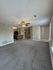 Spacious living area with modern ceiling fan and new carpeting, flowing into a kitchen with sleek appliances.