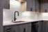 Modern kitchen with sleek gray cabinets, chic white countertops, stainless steel dishwasher, and contemporary black faucet.
