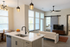 Modern open-concept living space with a stylish kitchen island, cozy seating area, and elegant pendant lighting, featuring large windows and a view into a serene bedroom.
