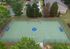 Vibrant aerial view of a spacious green sports court, surrounded by lush trees and modern residences, ideal for active living in a serene neighborhood.
