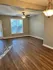 Bright and spacious living area with elegant wood flooring, large window, and modern ceiling fan, perfect for cozy family gatherings.