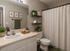 Inviting bathroom with modern white vanity, elegant shelving with decor, and a cozy ambiance featuring green plants and a lit candle.