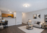 Cozy open-plan living room with stylish decor, featuring a comfortable sofa, modern artwork, and a home office nook adjacent to a compact kitchen.