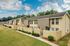 Charming townhouse row with private gated patios and lush green lawns under a vibrant blue sky, offering modern living in a serene environment.