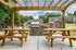 Charming outdoor picnic area with wooden tables under a pergola, featuring a modern grill and poolside view at a stylish apartment complex.