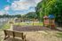 Inviting apartment community with a vibrant playground, cozy benches, and a refreshing pool surrounded by lush greenery, perfect for family fun.