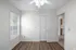 Bright room with elegant wood flooring, modern ceiling fan, and abundant natural light from large windows, adjacent to a kitchen space.
