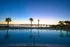 Serene apartment poolside view at sunset with palm trees and waterfront backdrop.