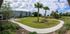Serene apartment complex with manicured lawns, palm trees, and a winding path under a vibrant blue sky.