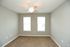 Bright and airy room with modern ceiling fan and plush carpet, featuring dual windows for natural light.